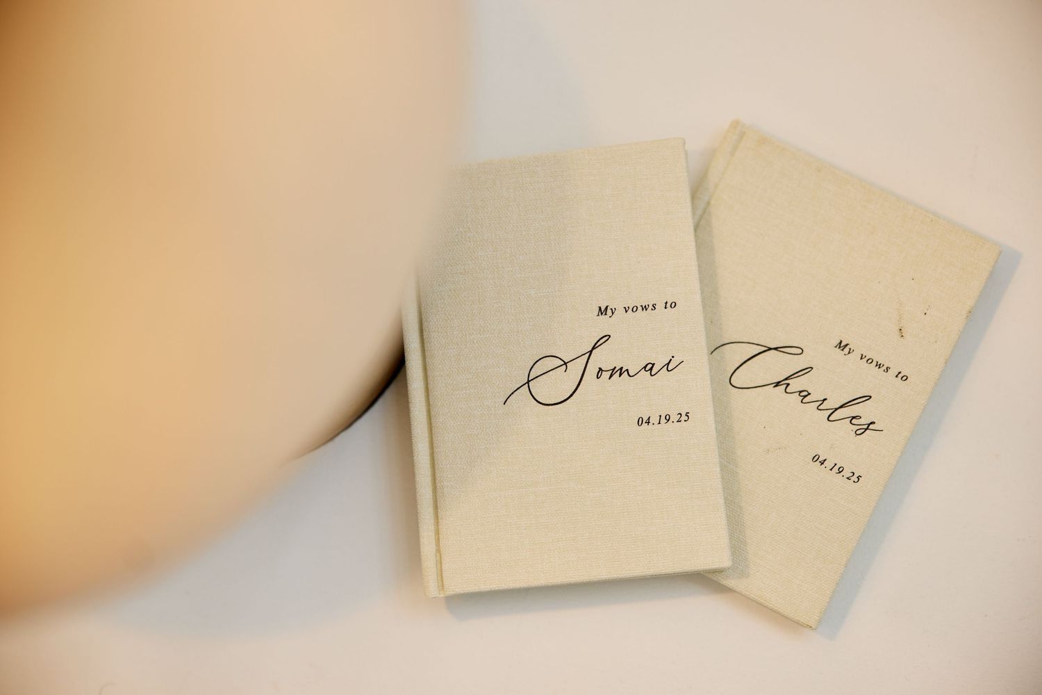 Two personalized wedding vow booklets for Somai and Charly dated 04.19.23 on a white surface.