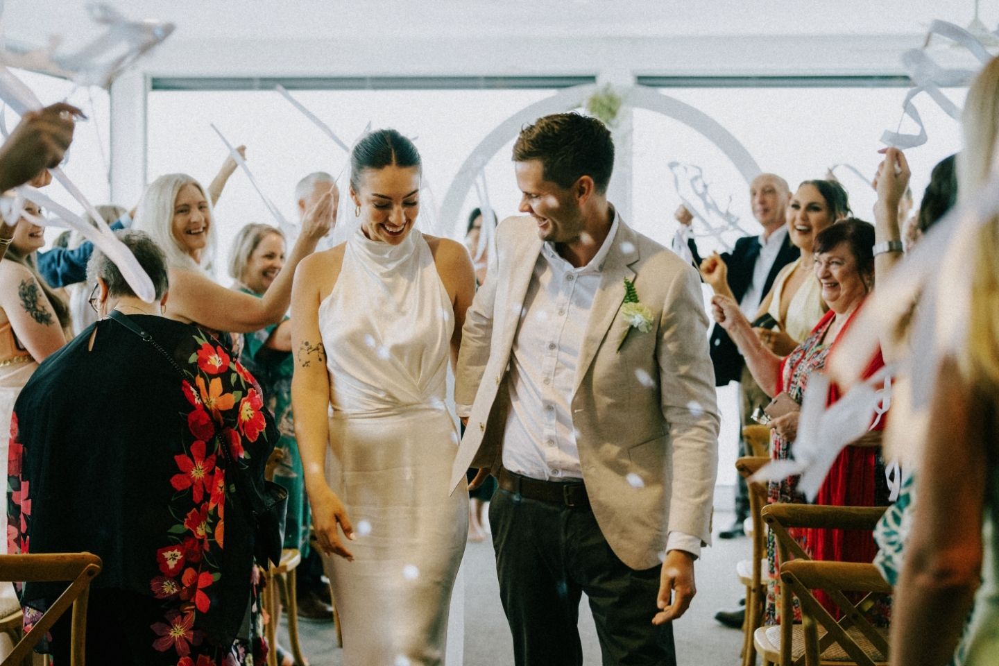 Bride and groom walk down the aisle as guests celebrate with streamers at an elegant outdoor wedding ceremony.