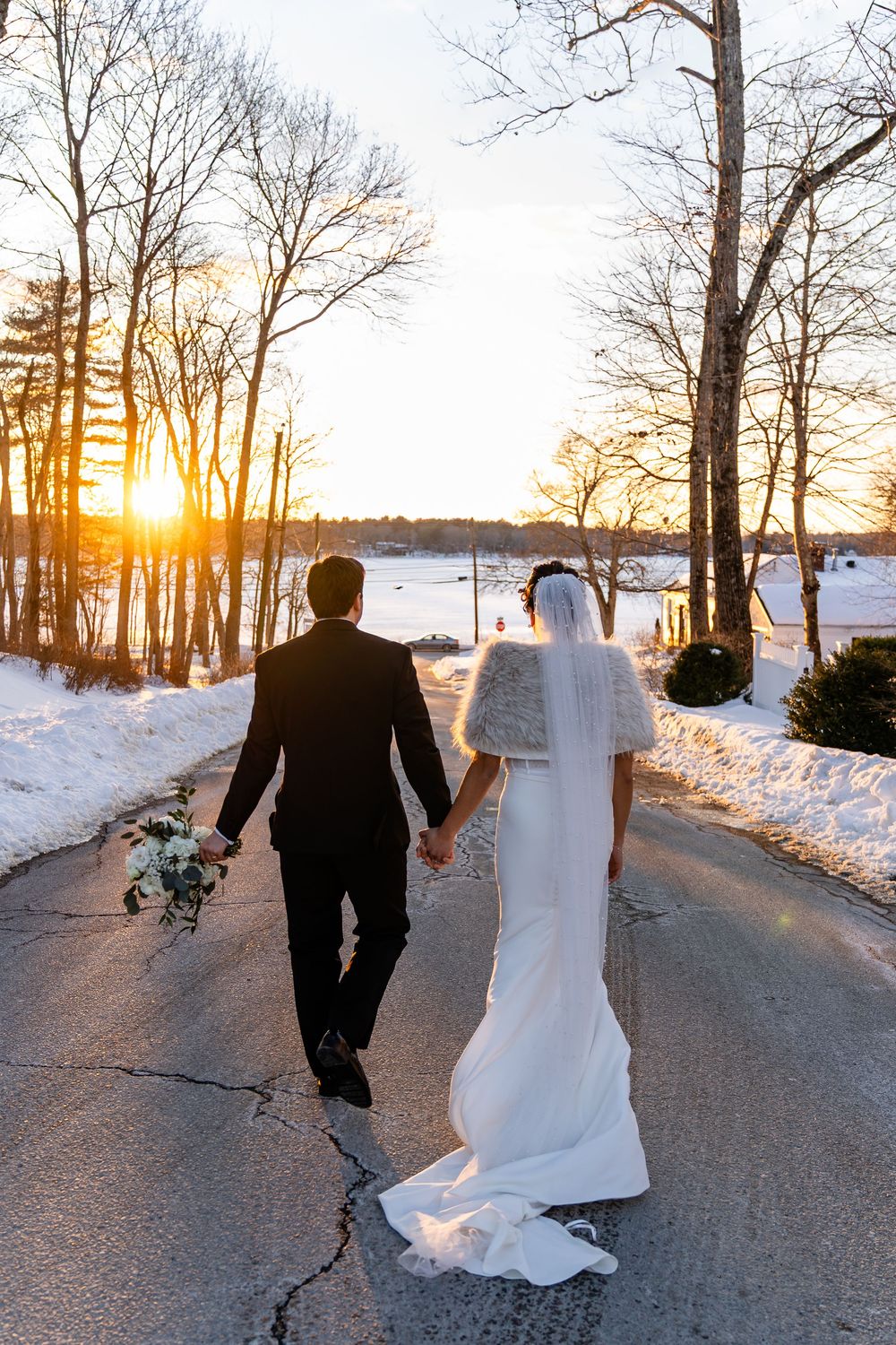Bride and groom walk hand in hand down snowy road at sunset at The Saphire Estate