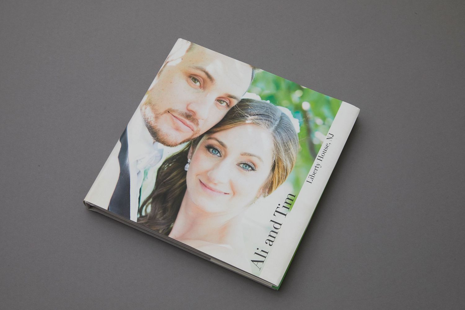 Square wedding photo book featuring a smiling couple on the cover, displayed on a gray background.