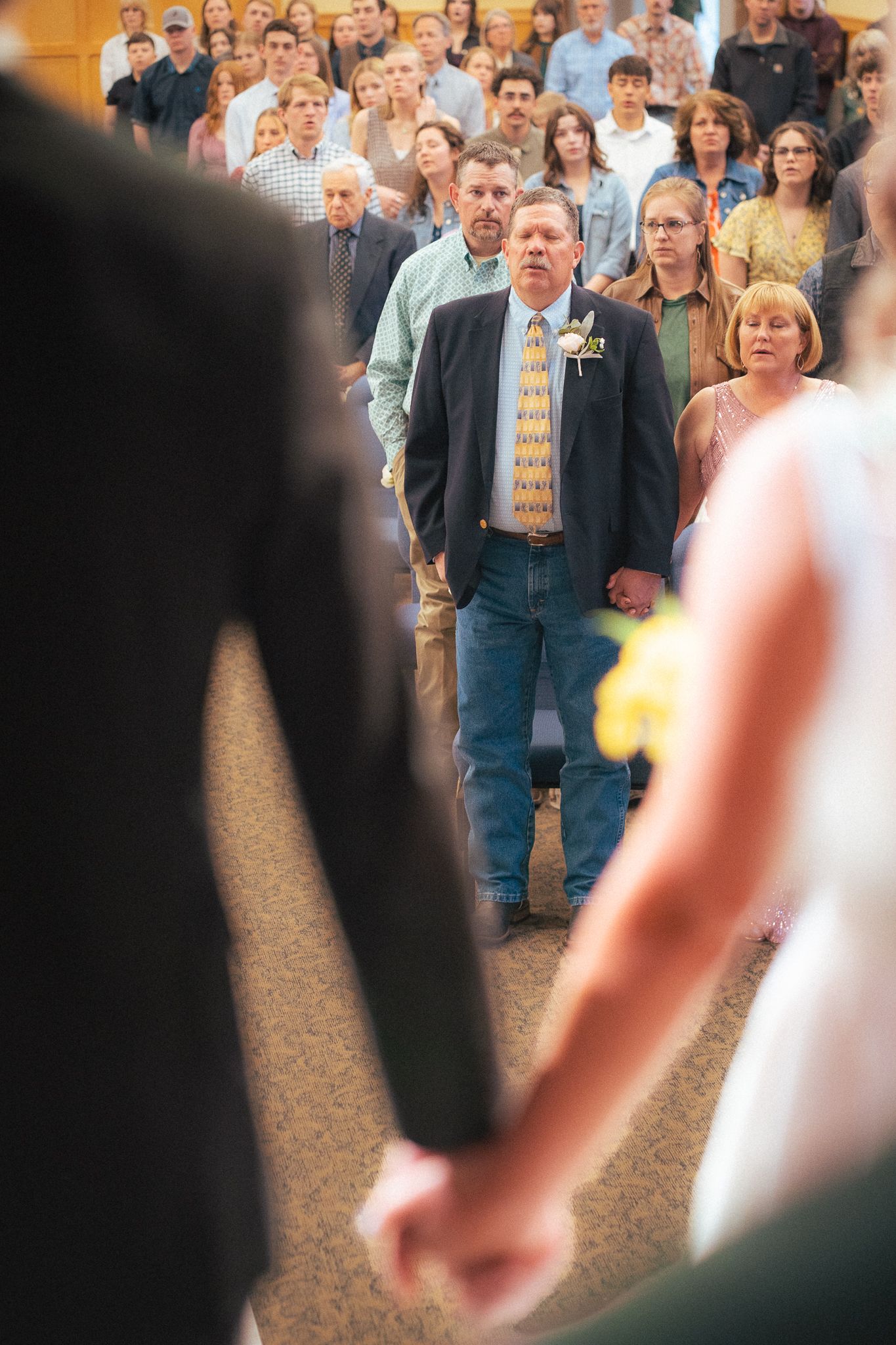 Bride and groom holding hands facing wedding guests during ceremony in a crowded venue.