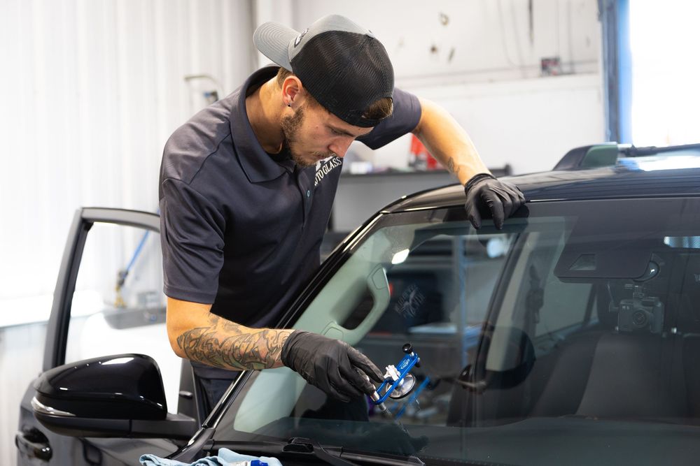 Auto technician in cap carefully applying tint film to a car window in a professional garage.