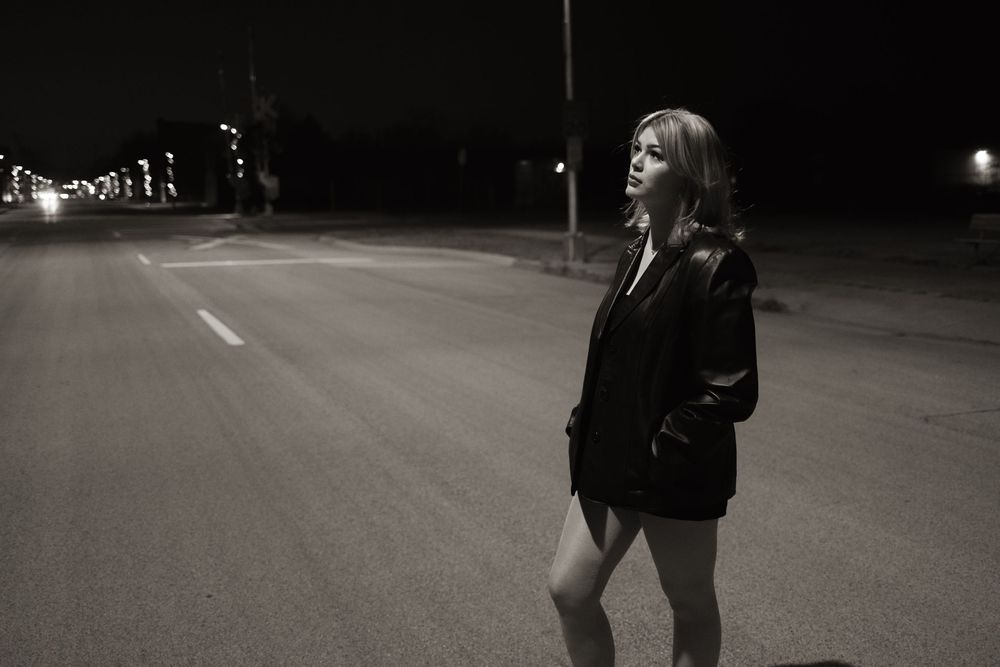 Woman in black jacket standing alone on empty road at night, black and white photography.