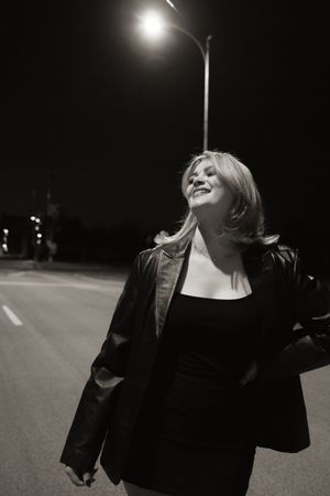 Black and white photo of a smiling blonde woman in leather jacket under a street light at night.