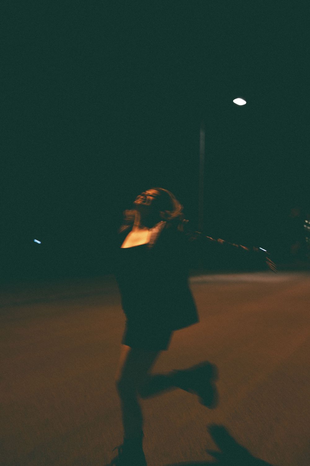 Blurred motion shot of a woman dancing freely under a street light at night on an empty road.