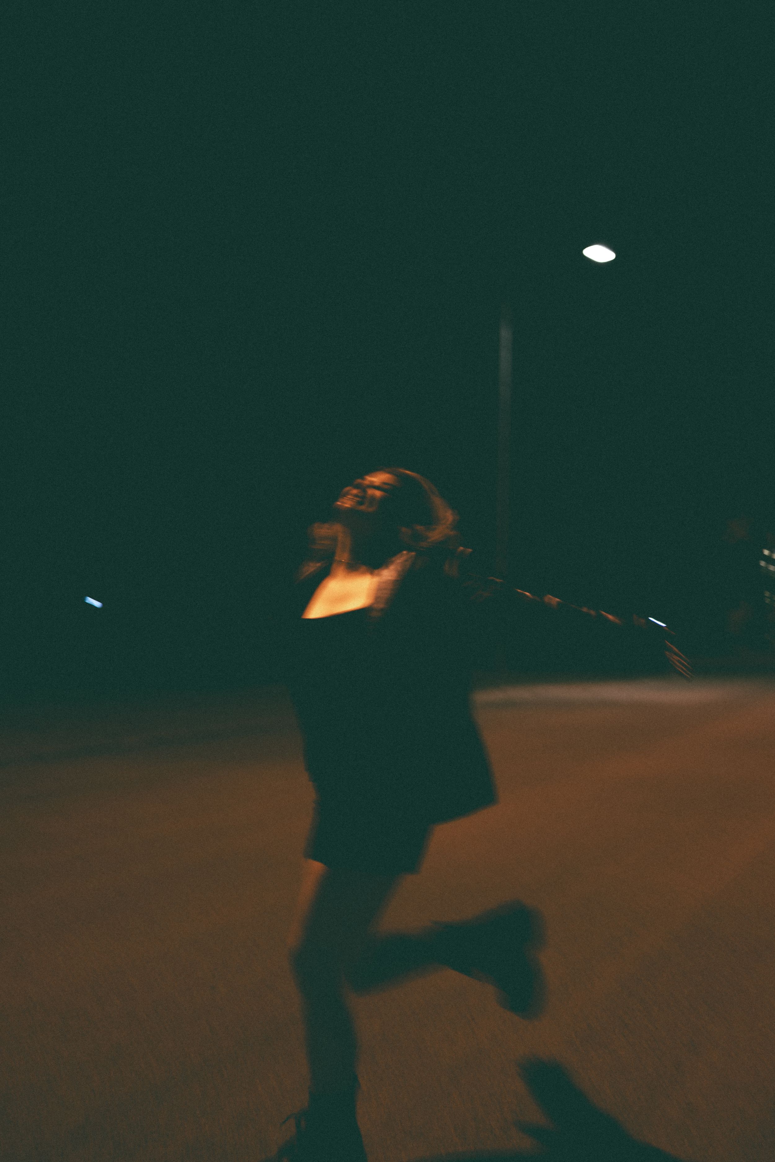 Blurred motion shot of a woman dancing freely under a street light at night on an empty road.