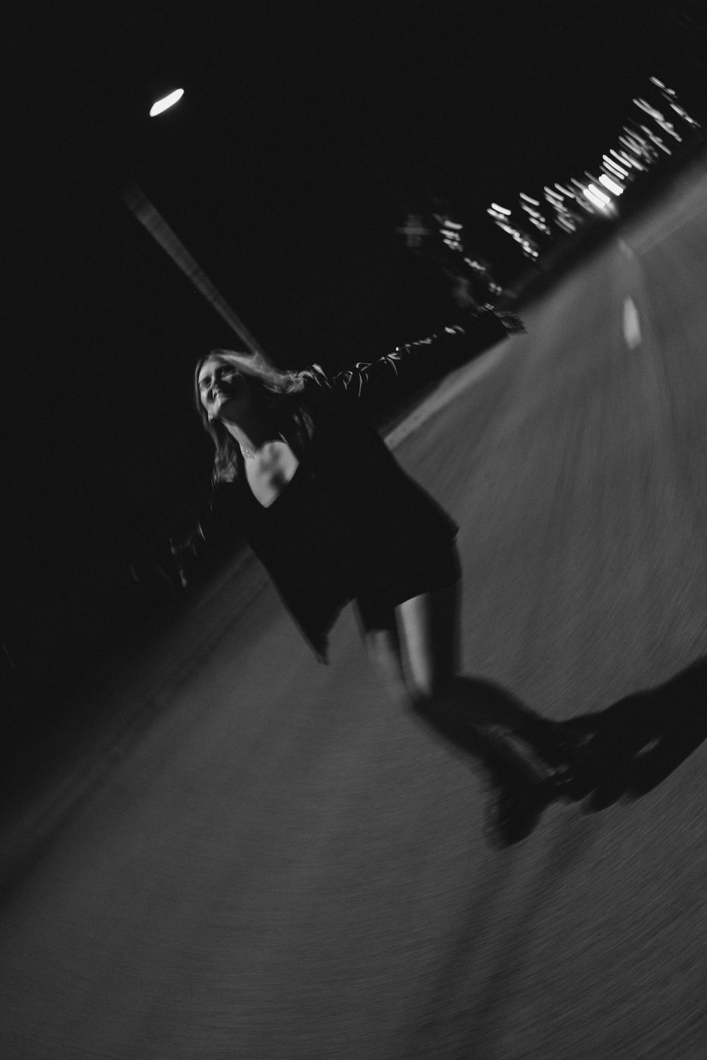 Blurred black and white photo of a woman skating at night on a ramp under a street light.