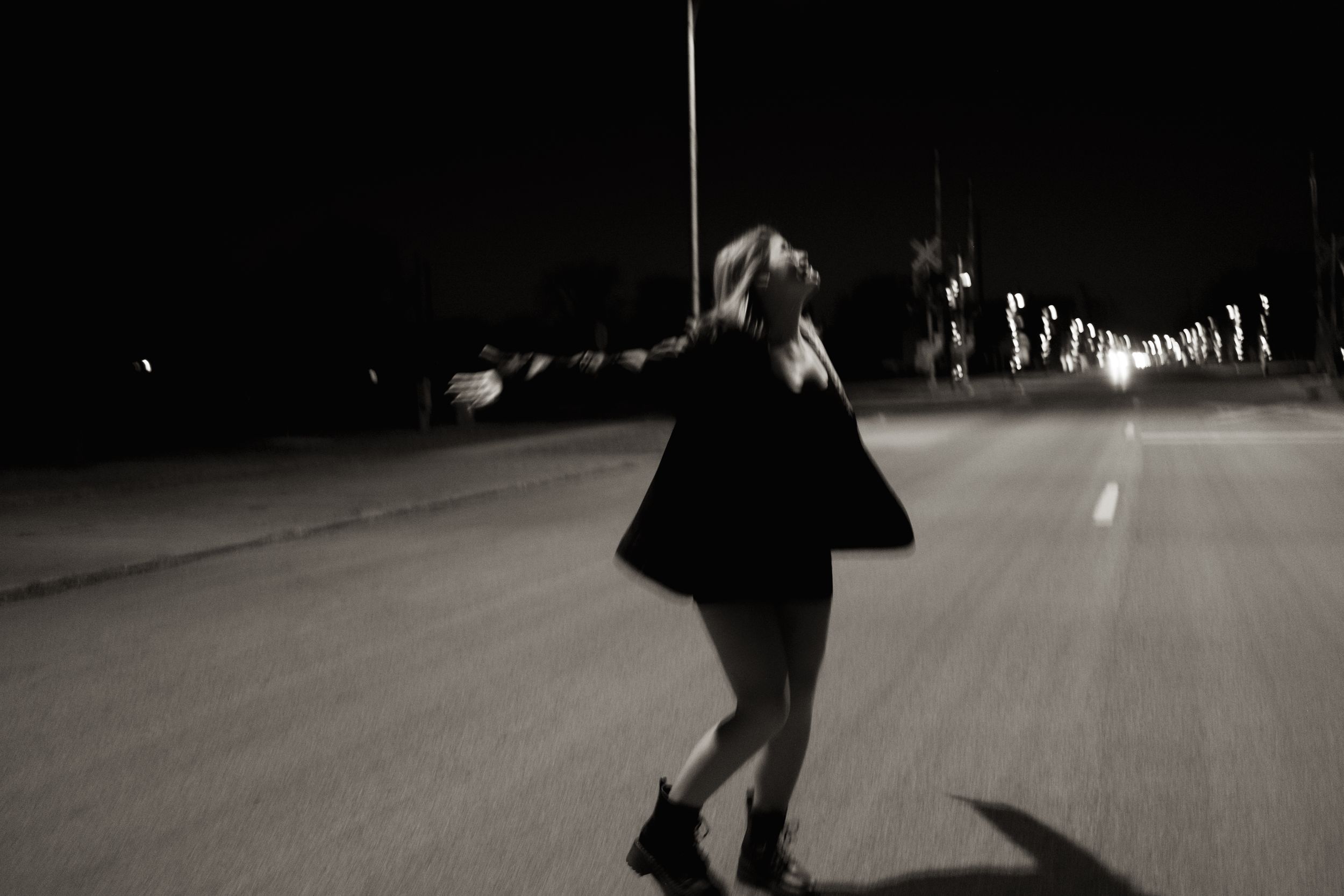 Blurred black and white image of a woman dancing alone on a dark empty road at night.
