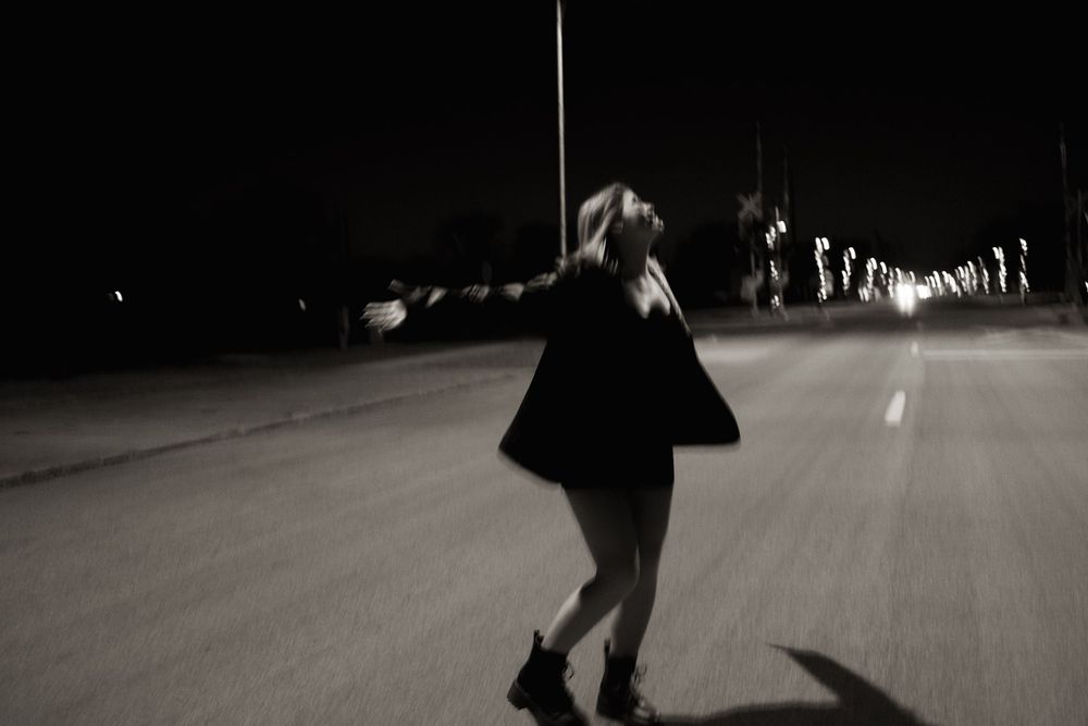 Blurred black and white image of a woman dancing alone on a dark empty road at night.