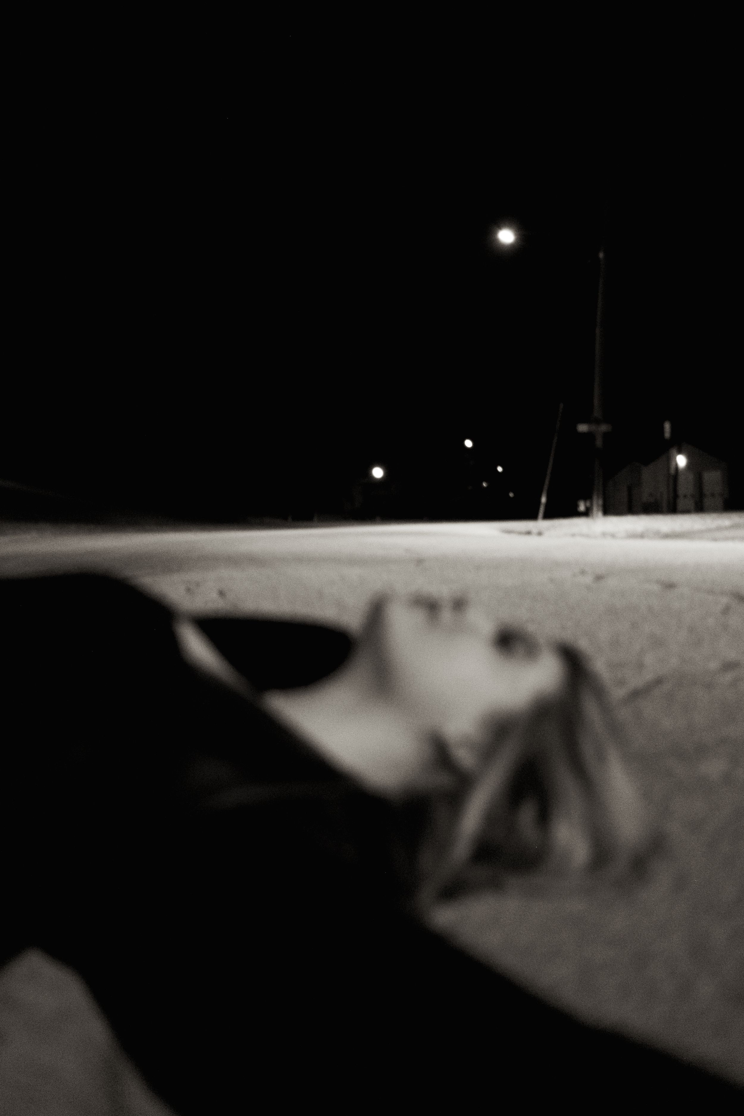 Black and white photo of blonde woman lying on empty road under street lamp at night.