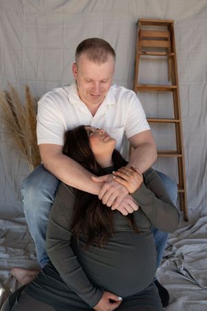 Couple sharing tender moment during maternity photo session with ladder backdrop.