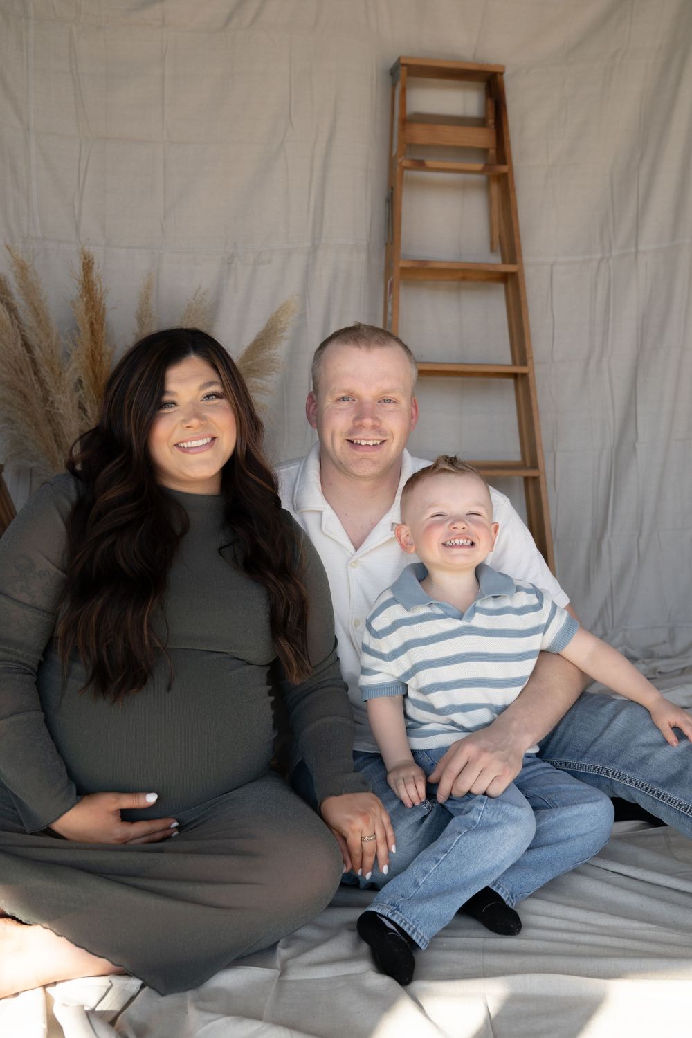 Smiling pregnant woman in green dress with husband and young son during maternity photo session.