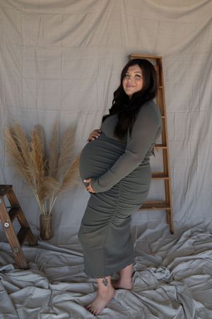 Pregnant woman in olive green ruched dress cradling baby bump during studio maternity photo session.