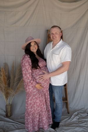 Smiling pregnant couple poses together in a studio maternity portrait with pampas grass decor.