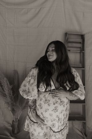 Black and white maternity photo of pregnant woman in floral dress cradling baby bump.