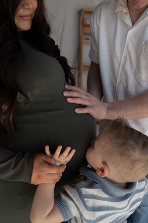 Pregnant woman in olive dress with toddler and partner touching baby bump during maternity photo session.