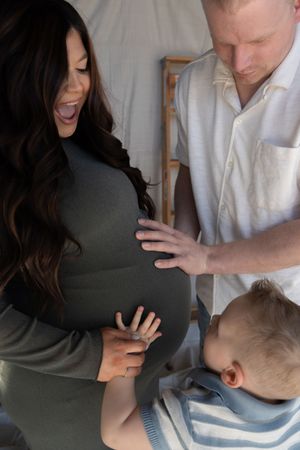 Pregnant woman laughing as toddler and man touch her baby bump during a family maternity photo session.