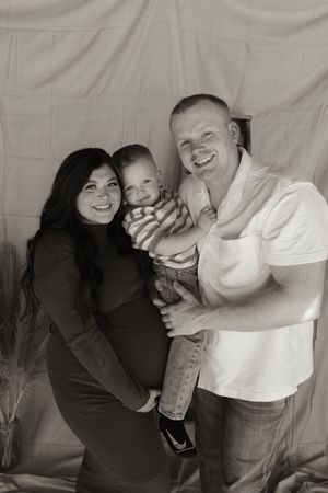 Happy family maternity portrait in black and white with pregnant mother, father, and toddler son.