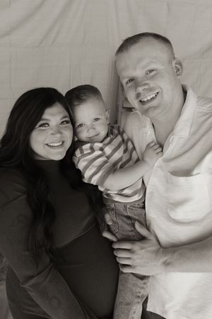 Black and white maternity family portrait with smiling couple holding their young toddler.