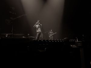 Black and white concert photo of a rapper performing on stage with a guitarist under dramatic spotlights.