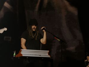 Long-haired musician performs on stage at a keyboard during a live concert.