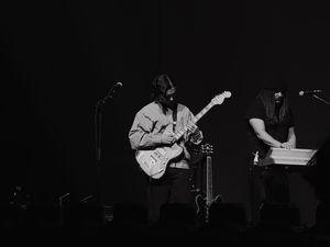 Black and white photo of a guitarist and keyboardist performing on a dimly lit concert stage.