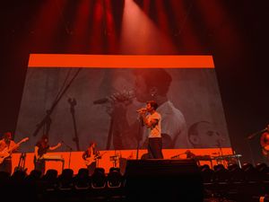 Concert stage with red lighting and large projection screen showing performers in silhouette.