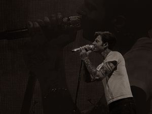 Tattooed male vocalist performing on stage with microphone in black and white concert photo.