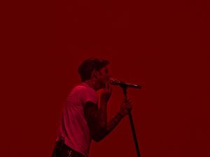 Male vocalist performing on stage bathed in dramatic red lighting while singing into a microphone stand at a live show.