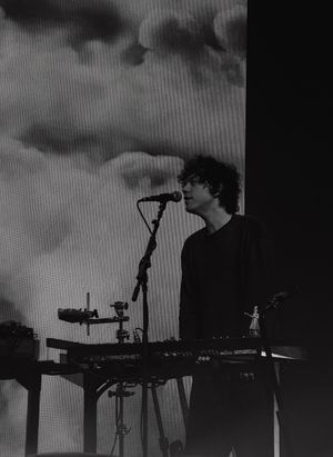 Musician playing synthesizer keyboard on dark stage at live concert in black and white photography.