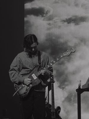 Guitarist playing electric guitar on stage with cloudy backdrop in black and white.