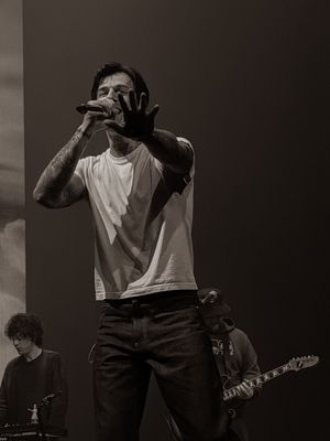 Tattooed rock singer reaching hand toward camera while performing live on stage in black and white.