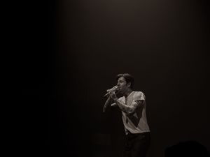 Male singer performing solo on a darkened stage holding a microphone in black and white.