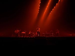 Band performing on stage under dramatic red lighting with multiple spotlights at live concert.