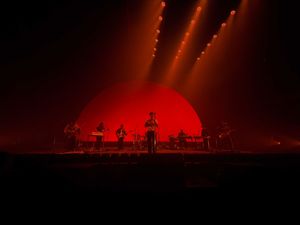 Band performing on stage with a large red semicircle backdrop and dramatic lighting.