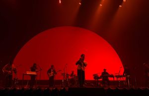 Band silhouetted against large red circular backdrop on concert stage with dramatic lighting.