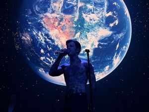 Singer performing on stage with a large illuminated Earth projection backdrop in a dark concert setting.