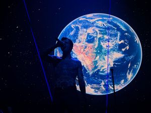 Silhouette of a person standing before a large illuminated Earth globe display against a starry blue background.