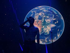 Silhouetted performer standing before a large illuminated Earth globe on stage.