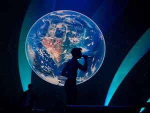 Silhouette of performer singing in front of large glowing Earth projection on concert stage.
