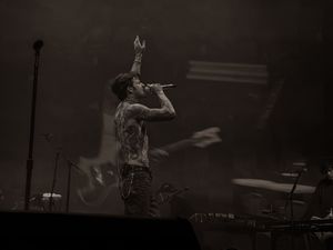 Shirtless tattooed male singer performing with microphone on smoky concert stage in black and white.