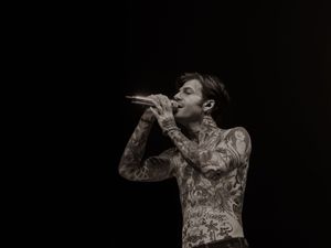 Shirtless tattooed male singer performing on stage, holding microphone to lips in black and white concert photo.