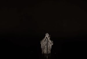 Dark moody black and white photo of a small illuminated figurine against a black background.