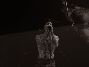 Shirtless tattooed male singer performing with hands clasped in dramatic black and white concert photo.