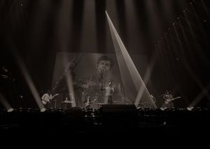 Band performing on large stage with giant screen projection and dramatic concert lighting in black and white.