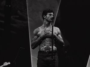 Tattooed shirtless male singer performing on stage in black and white photo.