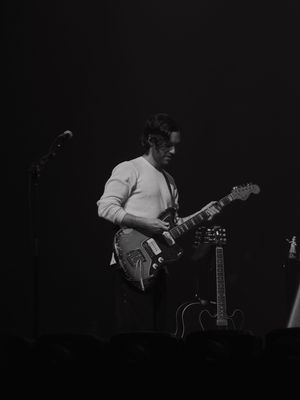 Black and white photo of a male guitarist performing on stage with a Fender guitar under dramatic lighting.