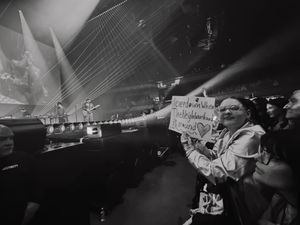 Fan holding a handwritten sign reaching toward the stage during a live concert.