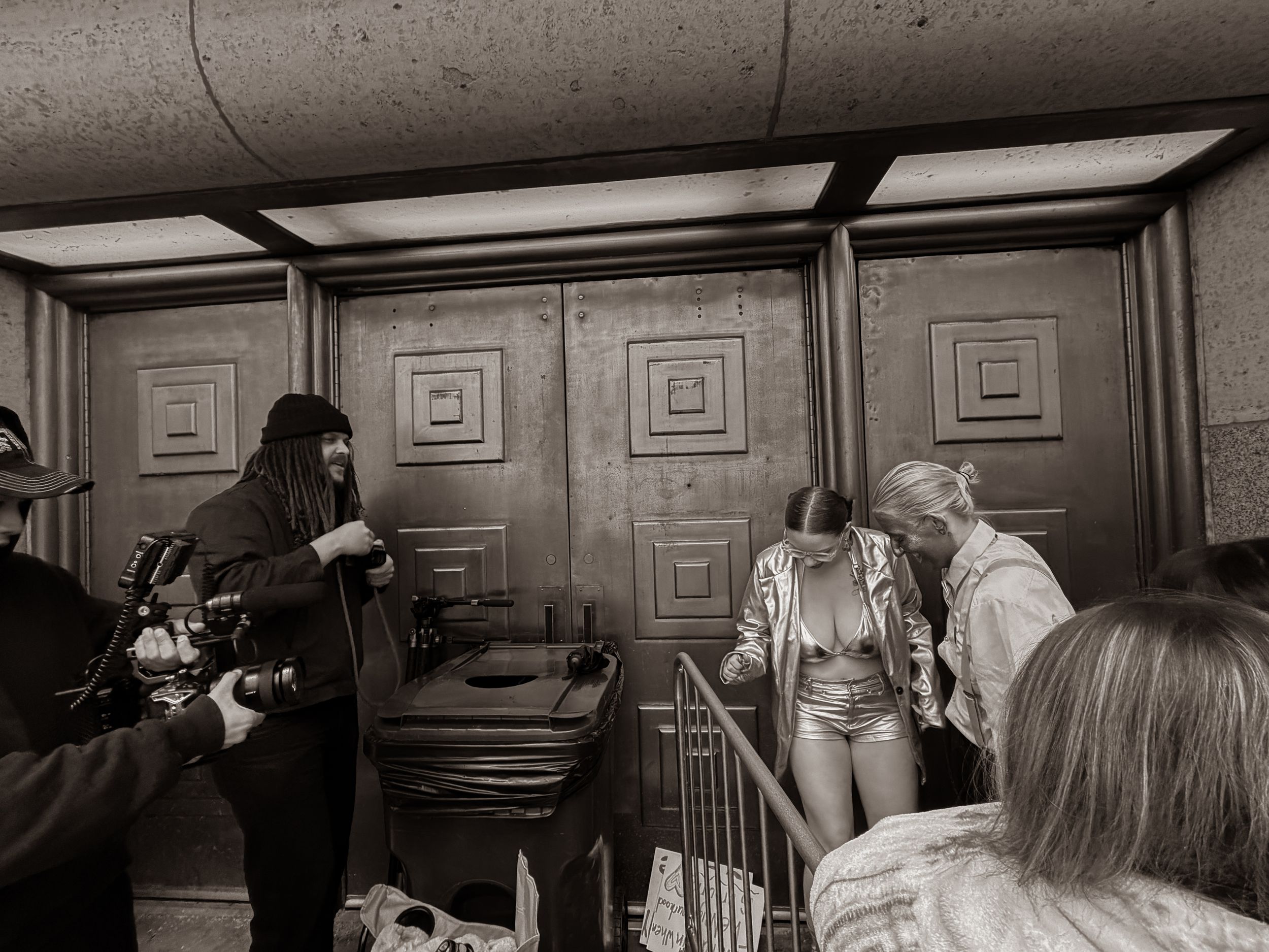 Black and white backstage photo of crew filming performer near ornate wooden doors.