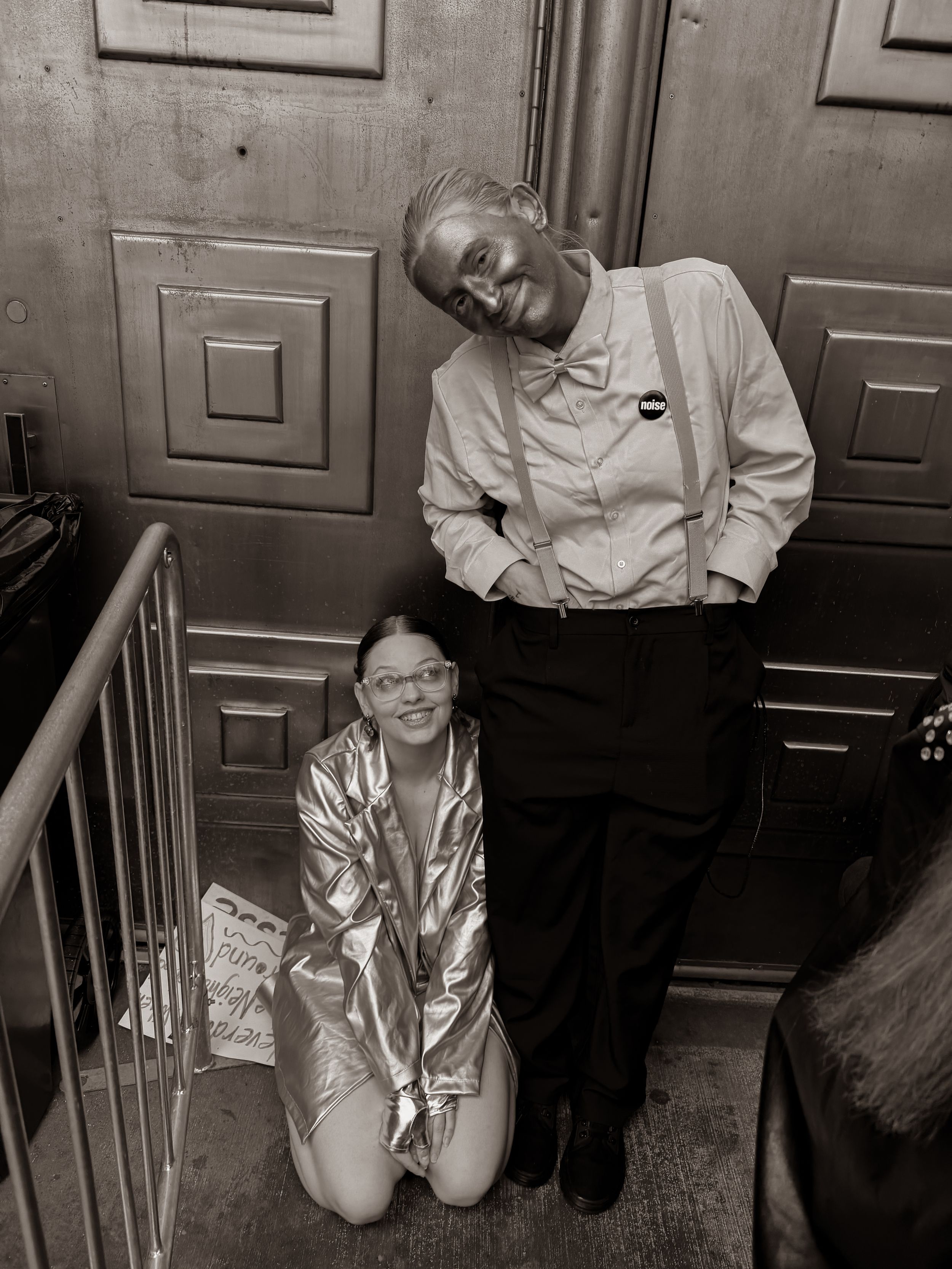 Black and white photo of two performers posing backstage, one in gold jacket kneeling.